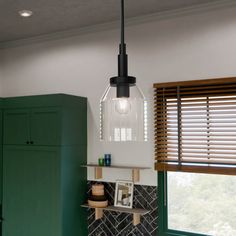 a kitchen with green cupboards and a hanging light over the stove top in front of a window