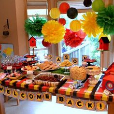 a table topped with lots of food next to a window filled with paper flowers and hanging from the ceiling