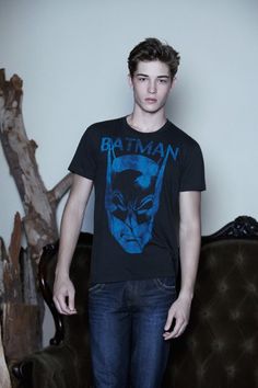 a young man standing in front of a couch wearing a batman t - shirt and jeans