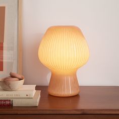 a lamp sitting on top of a wooden table next to books and a bowl in front of it