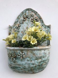 yellow flowers are placed in an old blue planter on a white wall behind it