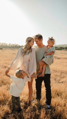 a family standing in the middle of a field with one holding their child and looking at the camera