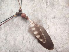 a feather and bead necklace on a stone surface with beads hanging from it's end