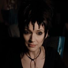 a woman with black hair is looking at the camera while she sits in a dark room