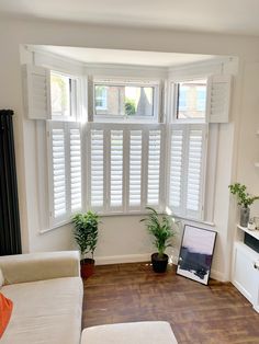 a living room filled with furniture and windows covered in white plantation shutters, along with a laptop computer on the floor