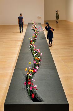 two people walking down a long hallway with flowers on the floor in front of them