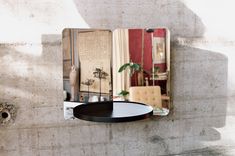 a mirror mounted to the side of a wall next to a table with a plant on it