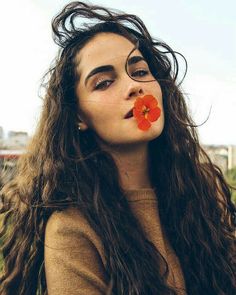 a woman with long hair and an orange flower in her mouth