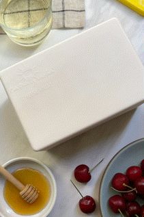 cherries and honey in small bowls on a white tablecloth next to a cutting board