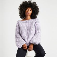 a woman sitting on top of a white chair wearing a purple sweater and black pants