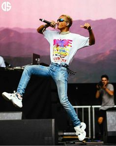 a male in a white t - shirt and blue jeans is doing a jump on stage