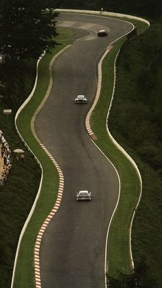 two cars driving down a winding road with grass on both sides