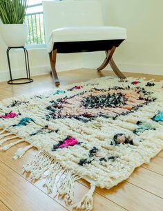 the rug is on the floor in front of a white chair and window with plants