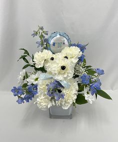 a blue and white flower arrangement with a teddy bear in it's centerpiece