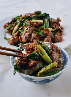 a bowl filled with meat and vegetables next to chopsticks on a white plate