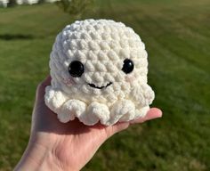 a hand holding a small white crocheted object with eyes on it's face