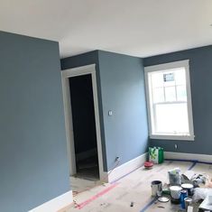 an empty room with blue walls and white trim on the floor, paint is being applied