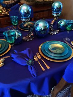 a table set with blue and gold plates, silverware and napkins on it