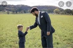 a man in a suit and tie holds the hand of a boy in a field