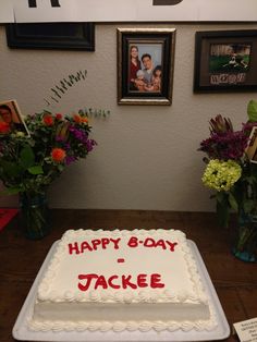 a birthday cake sitting on top of a wooden table next to vases with flowers