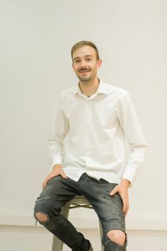 a man sitting on top of a stool with his hands in his pockets while wearing ripped jeans