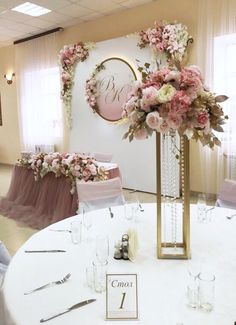 a white table topped with a tall vase filled with pink flowers next to a sign