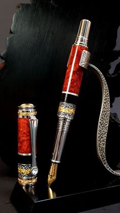 a red and silver fountain pen sitting on top of a black table next to a metal object