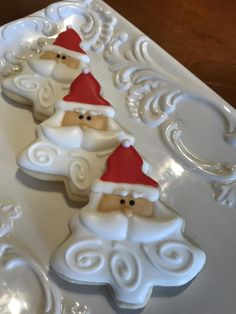 three santa clause cookies sitting on top of a white platter with swirly icing