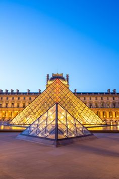 the pyramid is lit up at night in front of a large building with many windows