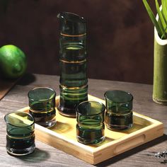 a wooden tray topped with glasses next to a green vase