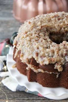 a bundt cake on a white plate with frosting and pecans in the background