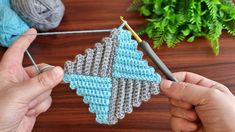 someone crocheting an ornament with yarn on a wooden table next to a potted plant