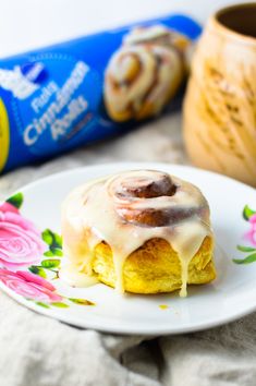 a cinnamon roll on a plate with icing drizzled over it and pink flowers