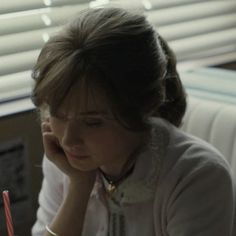 a woman sitting at a table writing on a piece of paper with a pen in her hand