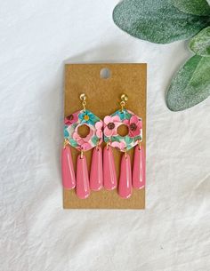 a pair of pink earrings with tassels and flowers on them sitting next to a potted plant