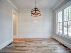 an empty room with wood flooring and white painted walls on the wall, along with a chandelier hanging from the ceiling