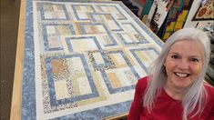 a woman with white hair standing next to a quilt