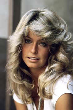 a woman with long blonde hair and blue eyes posing for a photo in front of a window