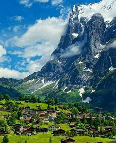 the mountains are covered in snow and green grass, with houses on either side of them