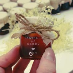 a hand holding a small jar with some flowers in it and a ribbon around the top