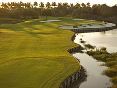 an aerial view of a golf course with water in the foreground and green grass on the far side