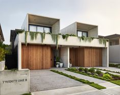 two story house with wooden garage doors and green plants on the front porch, surrounded by concrete planters