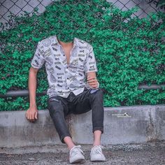 a man sitting on top of a cement wall next to a green plant covered fence