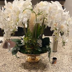 white flowers in a gold vase on a table with candles and other items around it