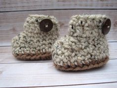 a pair of crocheted baby booties with brown buttons on them sitting on a wooden surface