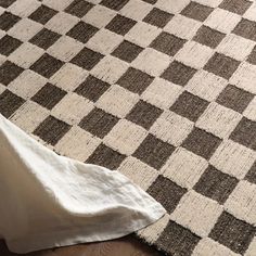 a brown and white checkered rug sitting on top of a wooden floor next to a bed