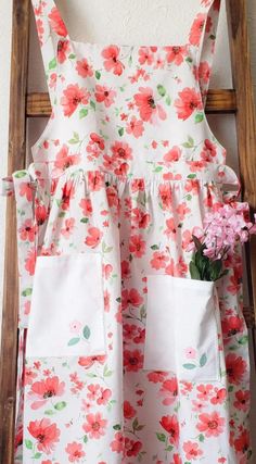 a flowered dress hanging on the wall next to a wooden chair with flowers in it