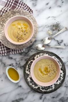 two bowls filled with soup on top of a marble counter next to silverware and spoons