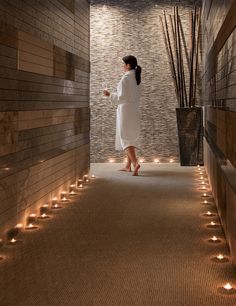 a woman in a bathrobe walking down a hallway with candles on the floor