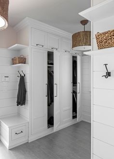 a white closet with some clothes hanging on the wall and two baskets in front of it